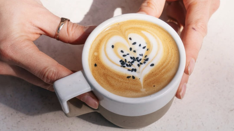 Person holding a coffee topped with black sesame seeds.