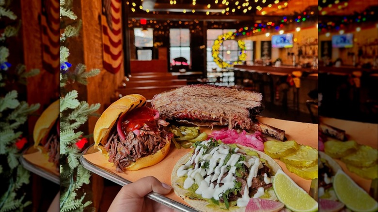 Hand holding tray with beef rib, sandwich, and taco