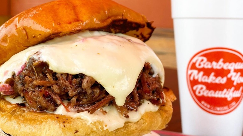 Slow Bone's Texas Nail sandwich with melty cheese and drink blurred in background