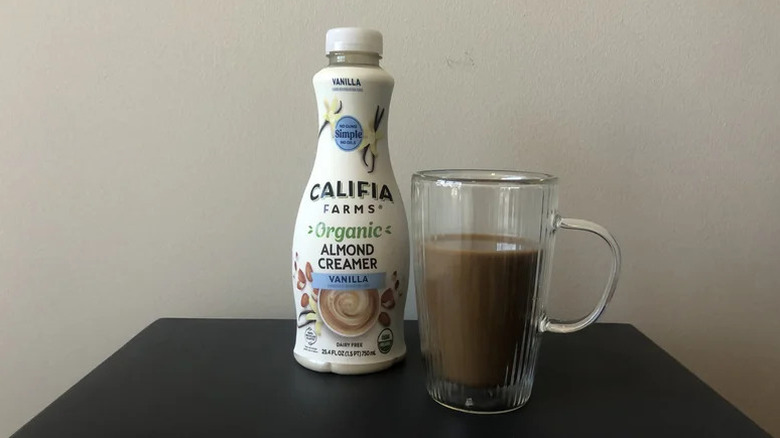 Califia Farms Organic Vanilla Almond Creamer on black table with a glass mug on the side filled with coffee
