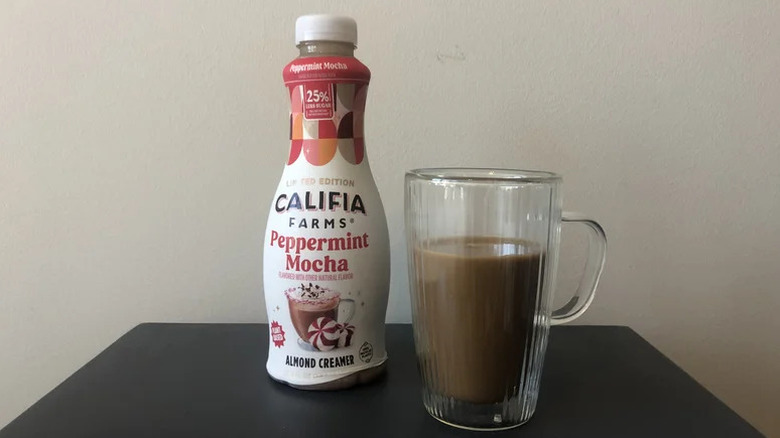 Califia Farms Peppermint Mocha Almond Creamer on black table with a cup of coffee