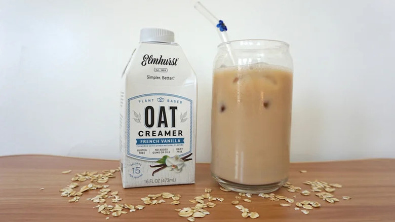 Elmhurst French Vanilla Oat Creamer on wooden table with a tall glass filled with milk and ice on the side