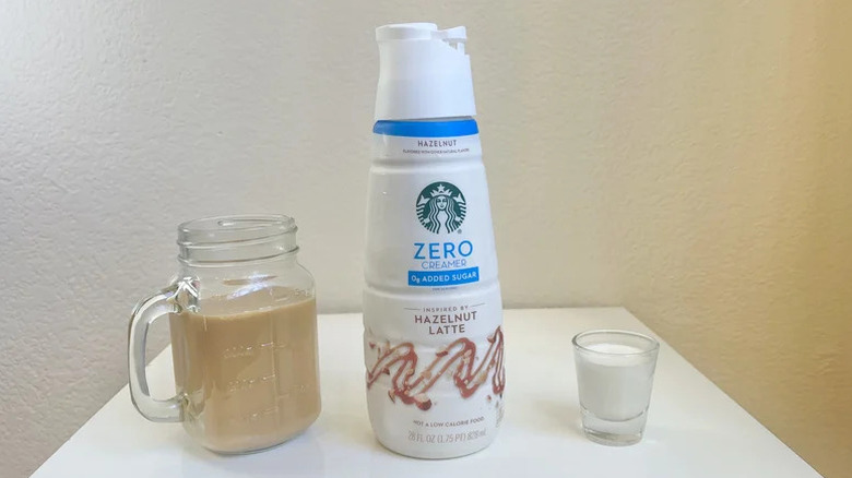 Starbucks Hazelnut Latte Zero Creamer with coffee on one side and a shot glass filled with creamer on the other side