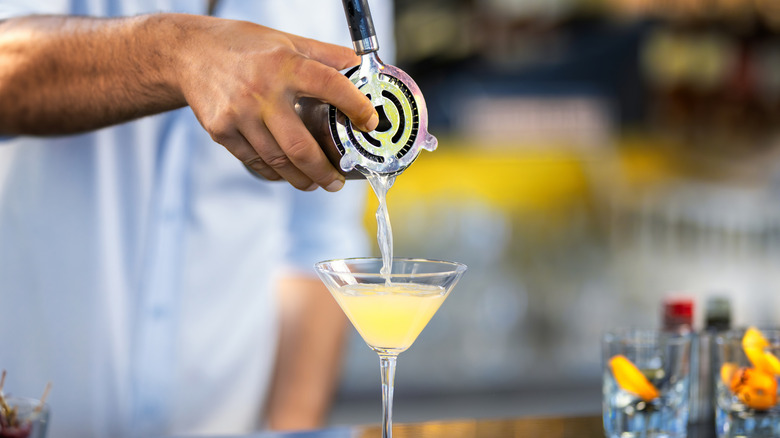 Someone pouring a martini into a glass