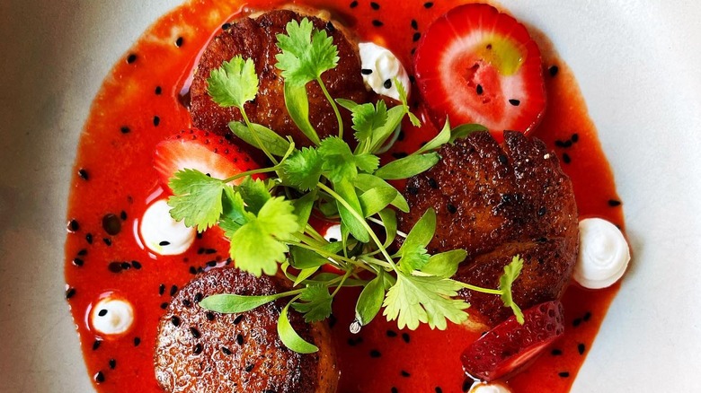 Seared scallops, strawberry, and aguachile on a white plate at La Fia Bistro
