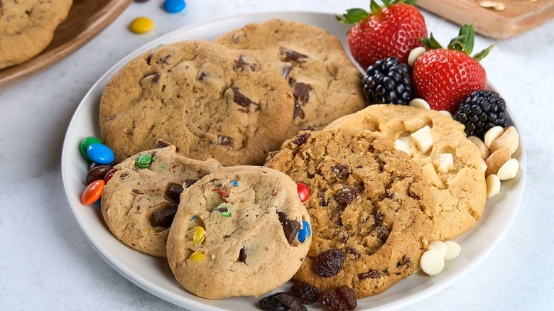 Four types of cookies on plate with strawberries, blackberries, raspberries, and pieces of candy