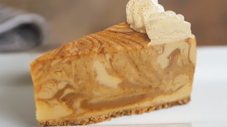 Slice of pumpkin cheesecake on plate topped with whipped cream