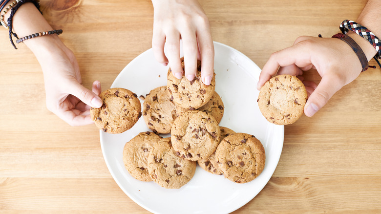 Three hands taking chocolate chip cookies from plate
