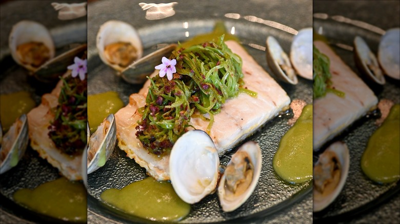 Fish dish with green sauce and seaweed on black plate