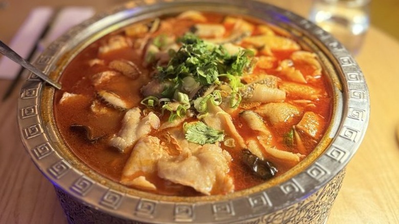 Sour fish soup in a metal bowl with chives on top