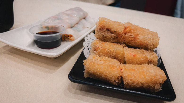 Crispy noodle rolls and steamed noodle rolls on a beige table with soy sauce