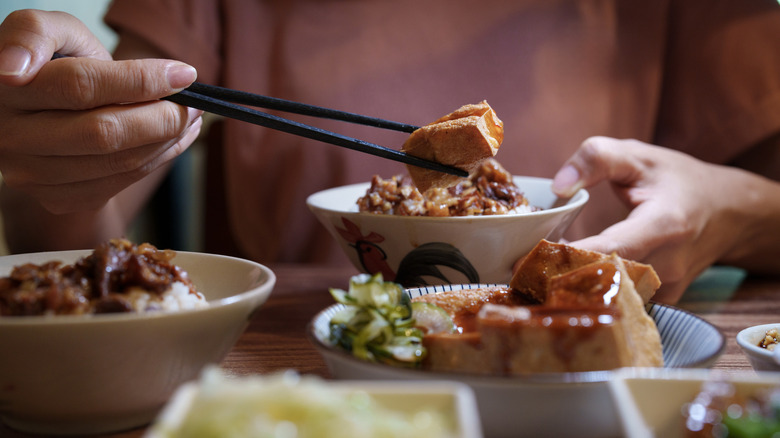 Hands holding Chinese food in bowl and chopsticks