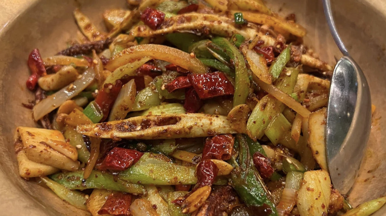 Spicy stir-fry in a clay pot with a silver spoon