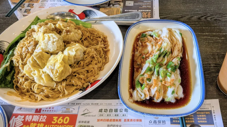 A plate of noodles with steamed wontons with a shrimp noodle roll on the side