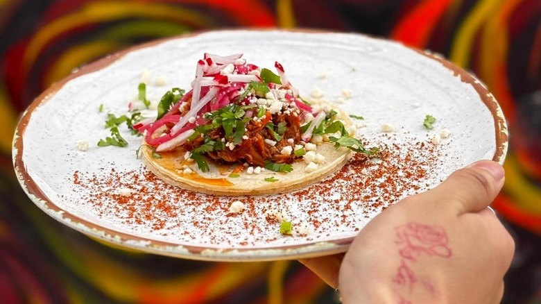 Hand holding white plate with spicy veal taco