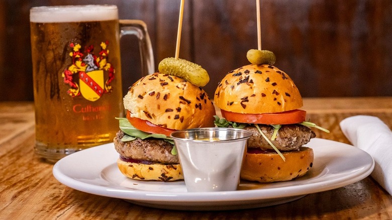 Two sliders on seeded buns on white plate, beer mug in background