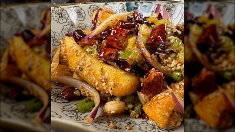 Close-up of fried dish with red onions, peppers, green onions, sesame seeds in bowl