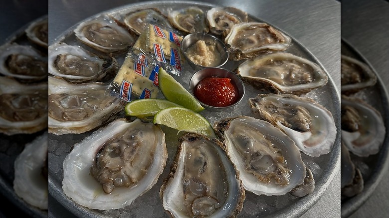 Close-up of oysters sitting on plate of ice, lime wedges and saltine crackers in the middle