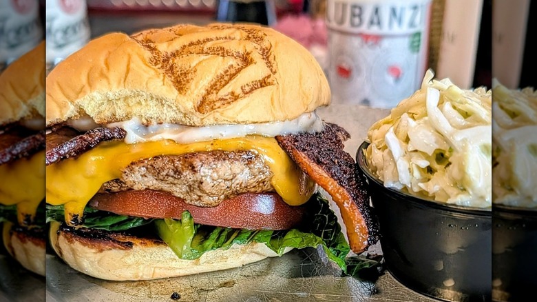 Turkey bacon burger with cheese, lettuce, tomato on bun next to cup of coleslaw