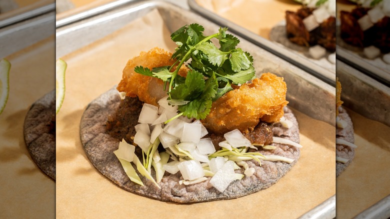 Close-up of fried fish taco from Taquiza Tacos on parchment-lined tray