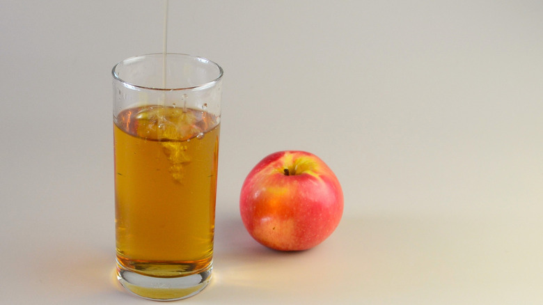 A glass of apple juice with an apple next to it