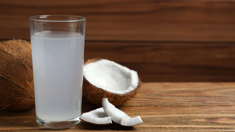 A glass of coconut water next to whole and cut coconuts