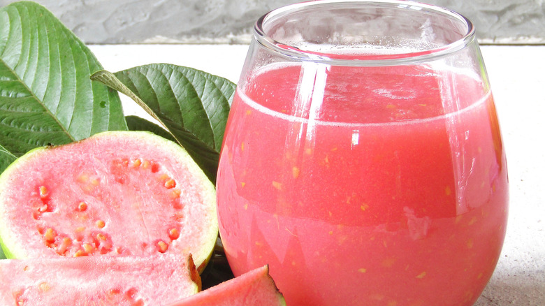 Pink guava juice in a glass alongside some guavas