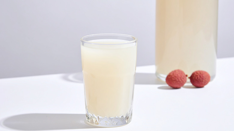 A glass of lychee juice with two whole lychees in the background