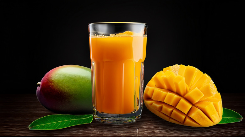 A glass of mango juice and mangoes on a black background