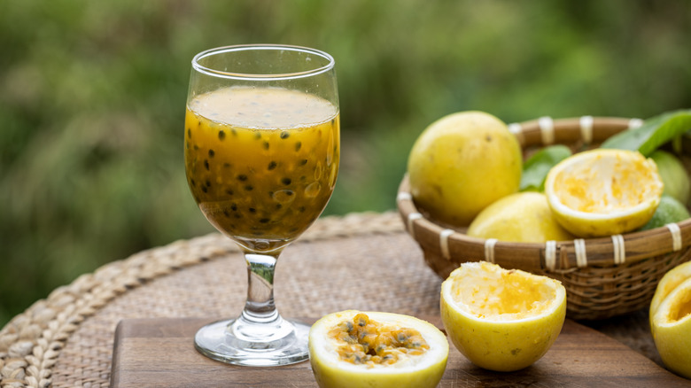 A glass of passion fruit juice with some scooped out passion fruits next to it