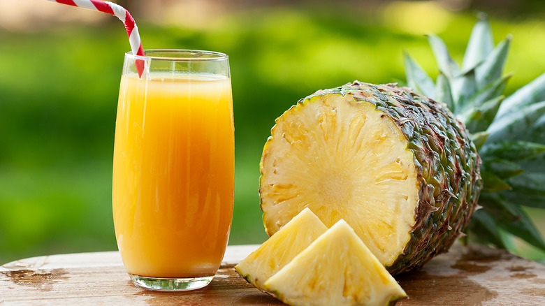 A glass of pineapple juice next to a cut open pineapple