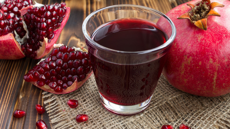 A glass of pomegrante juice with pomegranate pieces alongside it