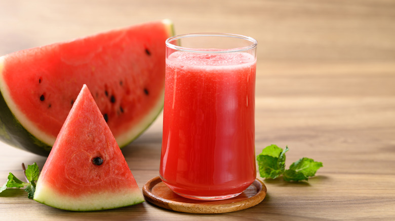 A glass of watermelon juice with some watermelon wedges