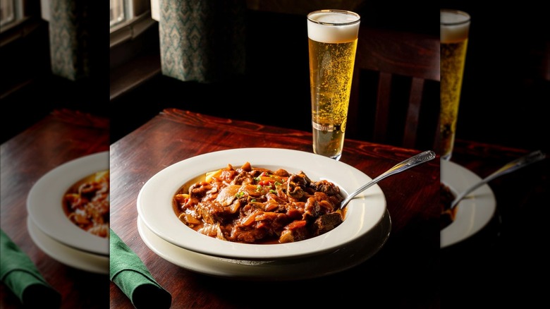 Bowl of goulash and glass of beer on table