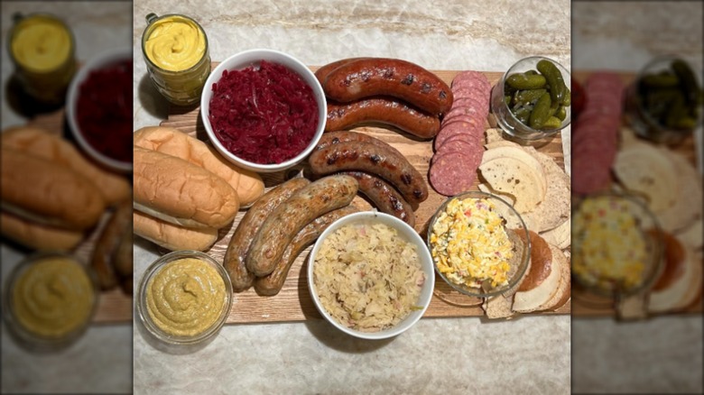 Wooden board with sausages, mustard, pickles, and sauerkraut