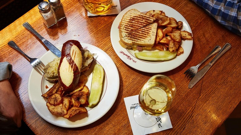 Plates with sandwiches, chips, and pickles on table with glass of white wine