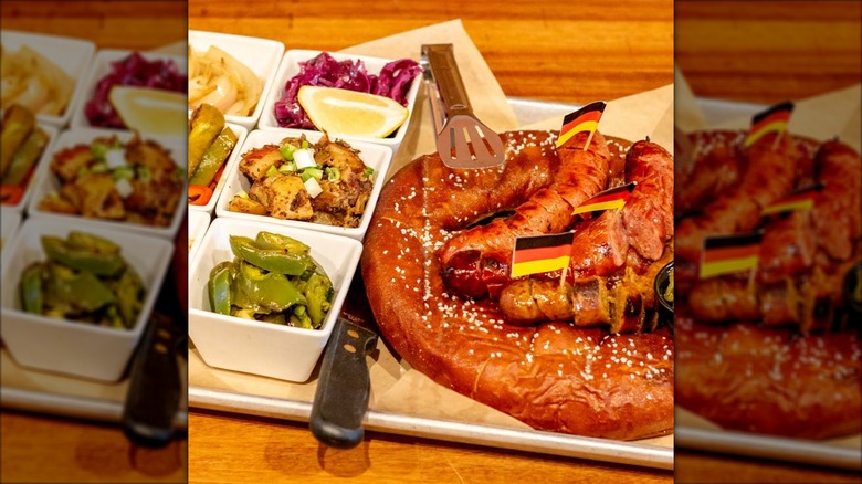 Soft pretzel on plate with sausages and side dishes of peppers and cabbage