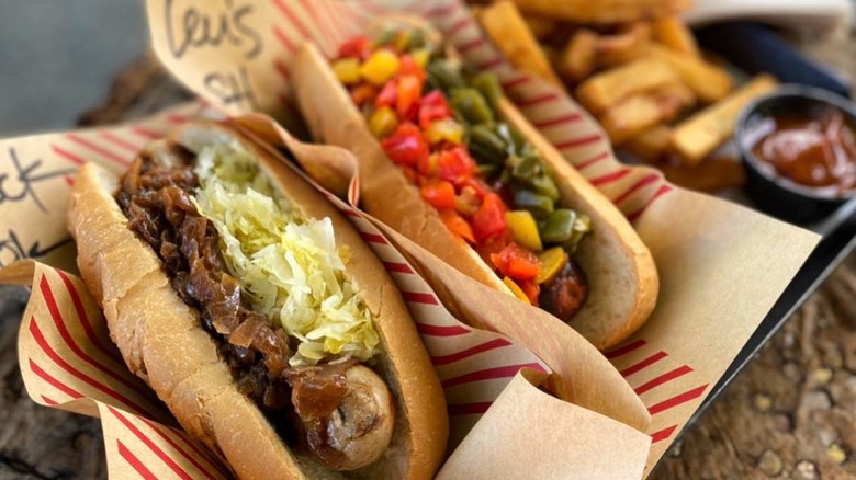 Two brats and buns on tray with paper, fries, and dipping sauce