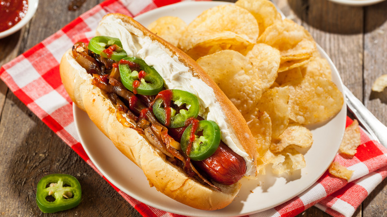 Seattle-style hot dog topped with jalapeños, on a plate with chips