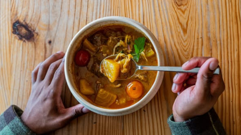 Hand holding a spoonful of West Indian curry in bowl on wooden table