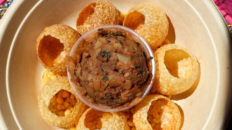 Plated pani puri with garbanzo beans, potatoes, and chutney mix in a bowl