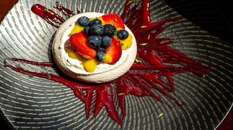 Pavlova with fresh berries, lemon, and meringue on dark plate