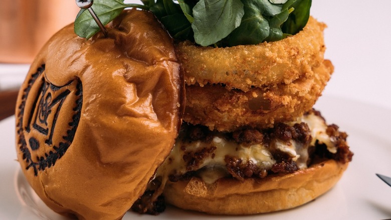 Burger with brie, bacon jam, and onion rings on plate