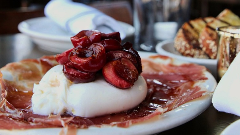 Plated prosciutto and burrata with cherries and evoo