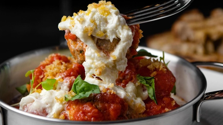 Fork and a bowl of meatballs with pomodoro, stracciatella, garlic, and bread crumbs