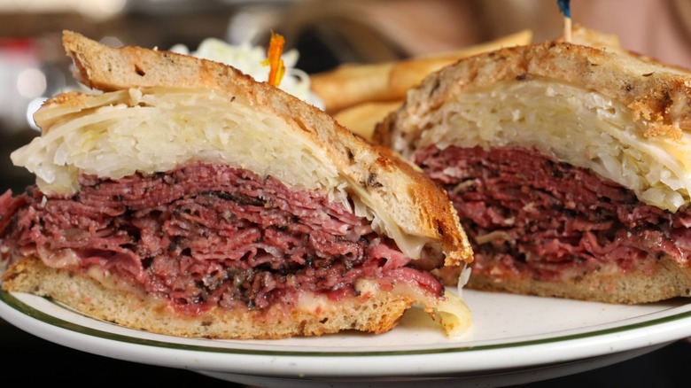 Two halves of a pastrami sandwich on white plate