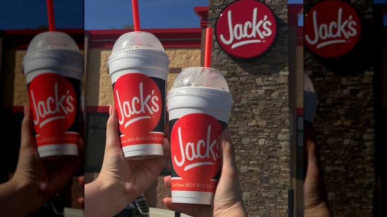 Hands holding up two Jack's milkshakes in front of the fast food restaurant