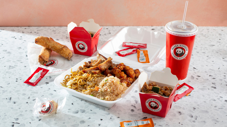 Food from Panda Express laid out on a table with a drink, fortune cookie, and condiment packets