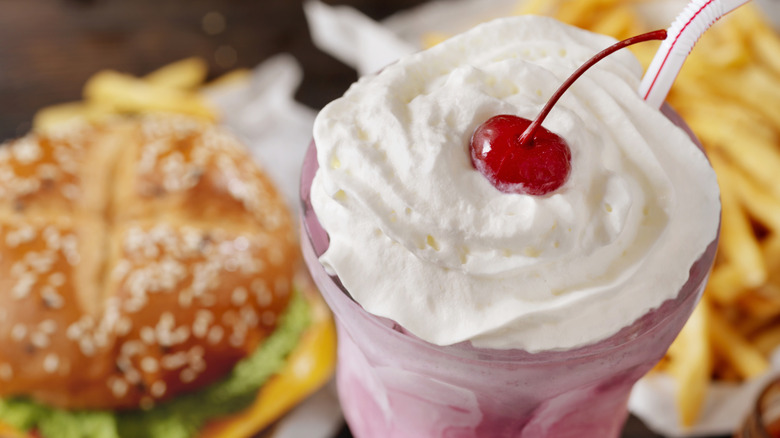A strawberry milkshake with whipped cream and a cherry