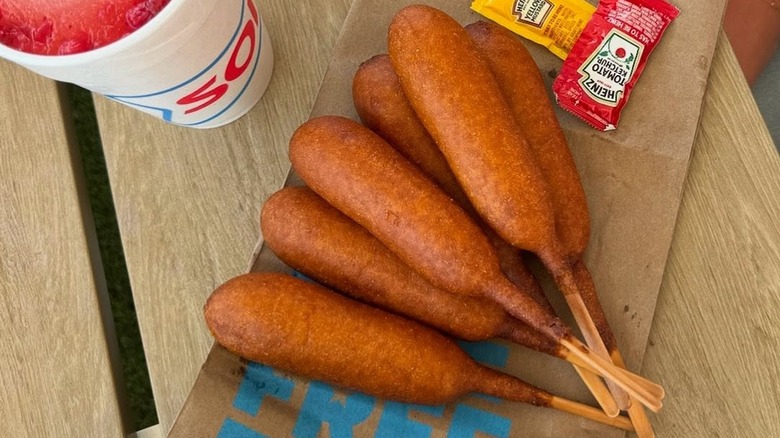 Corn dogs from Sonic arranged on a table next to a Sonic drink and condiment packets